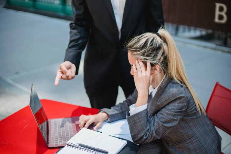 Business professionals discussing work on a laptop at an outdoor red table.